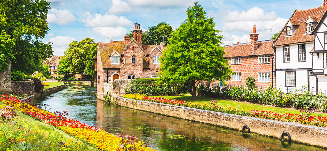 Vista de casas y edificios típicos en Canterbury, Inglaterra. Flores y árboles a lo largo del canal en verano.